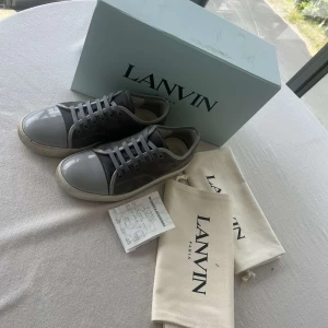 Gråa Lanvin skor - Snygga sneakers från Lanvin i grå mocka med grå lackad tå. Snörena e helt nya o oanvända eftersom jag bytte ut dom innan jag la upp annonsen. Storlek UK7 och EU42-43. Har tvättat och borstat med en mocka borste så att dom har hållt sitt material i bra skick och har sprayat dom med impregnerings spray innan jag la upp dom. Köpte skorna från NK Göteborg i Januari så har inte använt under en lång period. Kvitto dustbags, box o allt og ingår som man får med via köp. Pris e 3299kr, går att diskutera.