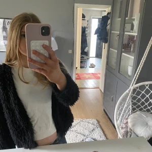 Svart pälsjacka i kort modell - Säljer en svart pälsjacka i kort, trendig modell. Jackan har lång ärm och är gjord i mjukt, fluffigt syntetmaterial som ger en cool look. Perfekt att slänga över en t-shirt för en snygg outfit.