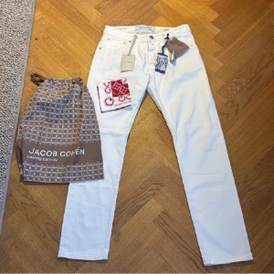Jacob Cohën Limited Edition - Exklusiva vita jeans från Jacob Cohën Limited Edition med röda detaljer och matchande rödvit bandana. Klassisk femficksmodell, rakt snitt och snygga kontrastsömmar. Kommer med originalpåse och accessoarer. Perfekta för dig som gillar stilrena och unika plagg. Aldrig använt, allt OG ingår. OBS JEANSEN ÄR FÖR LÅNGA FÖR MODELLEN I BILDEN OCH HAR EJ TAGITS TILL SKRÄDDARE.