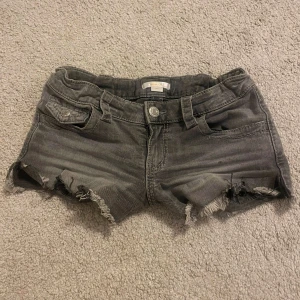 Grå jeansshorts från Gina Tricot - Snygga grå jeansshorts från Gina Tricot med låg midja och slitna, fransiga kanter. Shortsen har fickor både fram och bak med coola knappdetaljer. Perfekta för en chill sommarlook. Inga defekter förutom att jag har klippt en slits på båda sidorna (bild 4). Knappt använda 💕