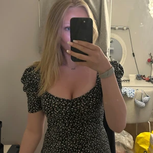 Svart blommig kortklänning - Supersöt svart kortklänning med små vita blommor, puffiga kortärmar och fyrkantig urringning. Sitter figurnära upptill och har en lätt utsvängd kjol. Perfekt för dig som gillar en feminin och trendig stil.