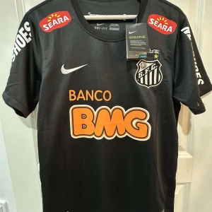 Santos Neymar Jr svart matchtröja Nike - Santos FC fotbollströja med Neymar Jr och nummer 11 på ryggen. Svart med vita och orange tryck, klubbmärke på bröstet och flera sponsorer. Tillverkad i lätt Dri-FIT-material som andas. Kortärmad modell, perfekt för dig som älskar brasiliansk fotboll.
