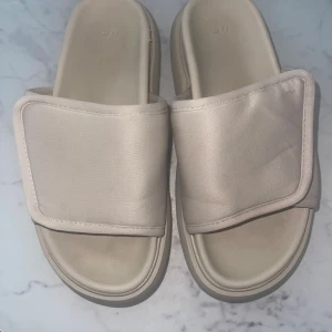 Beiga slides  - Chunky beiga slides från H&M med bred rem över foten och öppen tå. Snygg minimalistisk look med platt sula och mjukt syntetmaterial. Perfekta för sommardagar eller chill hemma. Enkel och clean design som passar till allt. MYCKET BEKVÄMA