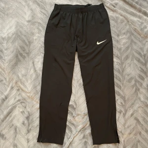 Nike träningsbyxor - Träningsbyxor från Nike i ett tunnt, plastigt och luftigt material. Byxorna är använda 1 gång och säljs då storleken inte passar. Skulle säga att dom passar någon som är mellan 170 och 178 cm lång.
