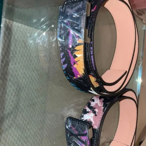  färgglatt skärp - Säljer ett  bälte . Bältet har ett färgstarkt mönster i svart, lila, rosa, gult och blått på utsidan och ljusrosa insida. Perfekt statement piece för att lyfta vilken outfit som helst.