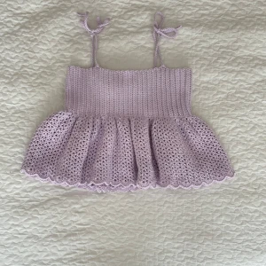 Virkad linnetopp med volang - Supersöt ljuslila egenvirkad linnetopp med knytbara axelband och volangig nederdel. Toppen har en ribbad överdel och en luftig, virkad kjoldel med vågig kant. Perfekt för sommarens alla tillfällen när du vill känna dig extra gullig. Storleken går att anpassa till viss del eftersom axelbanden kan justeras. 