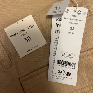 Beige low waist cargo jeans Gina Tricot - Snygga beige cargo jeans från Gina Tricot i low waist-modell. Byxorna har flera praktiska fickor på sidorna och bak, samt klassiska bälteshällor. Perfekta för en avslappnad och trendig look. Materialet är mjukt och skönt bomullstyg.