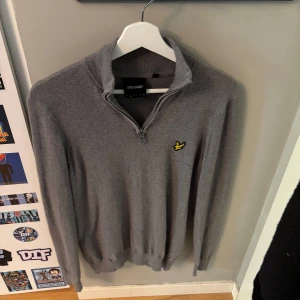 Grå half zip tröja från Lyle & Scott - Snygg grå långärmad tröja från Lyle & Scott med half zip och klassisk gul logga på bröstet. Tröjan har ribbade muddar och hög krage, perfekt för lager-på-lager-stil. Skön och stilren för dig som gillar enkel men clean look.