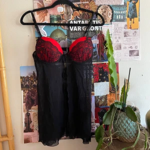 Svart och röd spetstopp - Säljer en topp med tunna axelband och röda kupor dekorerade med svart spets. Den har en liten rosett framtill och är tillverkad i ett tunt, transparent material som ger en lätt och luftig känsla. Ingen lapp i den men passar någon med storlek 38/40, B kupa!