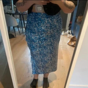 Blommig blå långkjol med slits - Säljer en snygg långkjol i blått med vitt blommönster. Kjolen har en rak passform och en slits på sidan som ger en extra cool touch. Perfekt för dig som gillar färg och mönster! Materialet känns lätt och flowy, perfekt för varmare dagar.