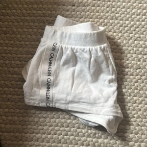 Vita lågmidjade shorts från Calvin Klein i bomull - Snygga vita shorts från Calvin Klein i mjuk bomull. Modellen är kort med elastisk midja och har logga längs sidorna. Perfekta för chill dagar eller strandhäng. Klassisk och clean look med sportig vibe. Äkta 