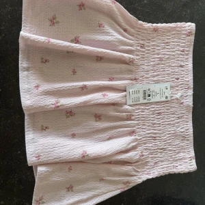 Ljusrosa blommig kortkjol från Gina Tricot - Supersöt ljusrosa kortkjol från Gina Tricot med små blommor i rosa. L men passar M också.