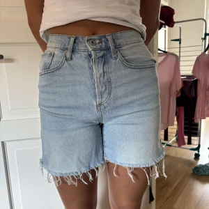 Ljusblå jeansshorts från Lager 157, XS - Säljer ett par ljusblå jeansshorts från Lager 157 i storlek XS. De är högmidjade med klassisk femficksdesign och har råa, fransiga benslut för en chill vibe. Perfekta för sommaren och lätta att matcha med allt. Snyggt slitna detaljer och skön passform.