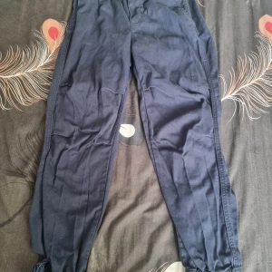 Mörkblå joggerbyxor från H&M - Mörkblå joggerbyxor från H&M med elastisk midja och muddar vid bensluten. Byxorna är pull-on-modell och har en avslappnad passform, perfekta för en chill vardagslook. Tillverkade i mjukt bomullsmaterial för extra komfort.