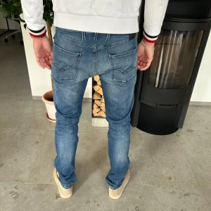 Replay Anbass blå jeans herr - Säljer ett par snygga Replay Anbass jeans i klassisk blå tvätt. Jeansen har raka ben, fem fickor och coola detaljer på bakfickorna. De är tillverkade i mjuk bomullsdenim med lite stretch för extra komfort. Perfekta för dig som gillar en stilren och modern look.