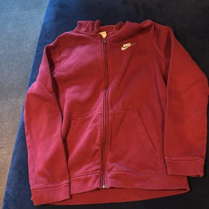 Röd Nike hoodie med dragkedja XL - Röd hoodie från Nike i storlek XL, med vit logga på bröstet och hel dragkedja framtill. Tröjan har huva, två fickor och är tillverkad i mjuk bomullsblandning. Perfekt för chill dagar eller när du vill ha en sportig look.