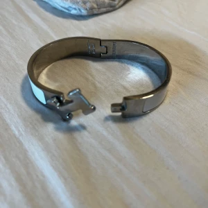 Vitt armband med silver H detalj - Snyggt armband i vitt med en silver detalj, måste få bort den så kom med bud