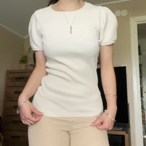 Beige ribbad topp med puffärm - Supersnygg beige ribbad topp från Carin Wester med puffiga korta ärmar och rund halsringning. Toppen har en slim passform och är gjord i ett mjukt, stretchigt material som sitter riktigt snyggt på kroppen. Perfekt att styla med jeans eller kjol. Står L men är så pass tight fit samt stretchig att den eventuellt passar allt från S och M till XL. 