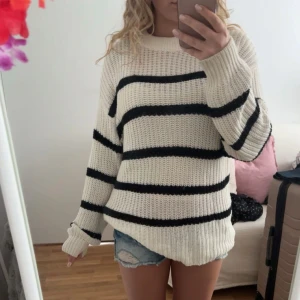 Randig stickad tröja  - Säljer en oversized stickad tröja i offwhite med svarta breda ränder. Tröjan har lång ärm, rund halsringning och är riktigt mjuk och skön. Perfekt för lager-på-lager och chill dagar.