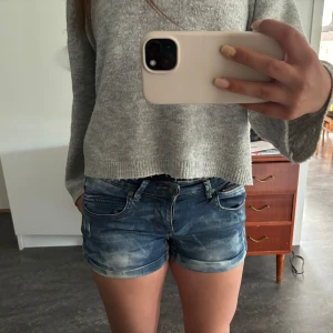 Blå jeansshorts från outfitters nation - Snygga blå jeansshorts med slitna detaljer och uppvikta benslut. Klassisk femficksmodell med dragkedja och knapp framtill samt extra dragkedjedetalj vid ena fickan. Perfekta för sommardagar och enkel att matcha med allt. Shortsen är i barnstorleken 158 men passar mig som har S i byxor.