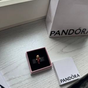 Pandora armband med två berlocker - Säljer ett snyggt Pandora armband i silver med en guldig hjärtformad låsdetalj. Medföljer två berlocker: en Iron Man i rött och guld samt en Stitch i silver med rosa öron. Perfekt för dig som älskar Marvel och Disney!