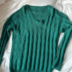 Grön stickad v-ringad tröja - Mysig stickad tröja i en djup grön färg med v-ringning och lång ärm. Tröjan har ett diskret mönster i stickningen som ger en snygg struktur. Perfekt att slänga på sig när det är kyligt ute.