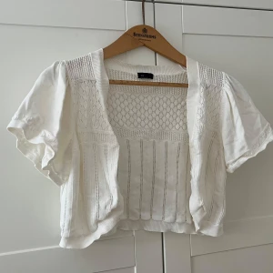 Vit stickad bolerotopp  - Supersöt vit bolerotopp från Lindex med korta puffärmar och stickade detaljer. Toppen har öppen front, vackert hålmönster och ribbade kanter. Perfekt att slänga över ett linne eller klänning för en extra touch.