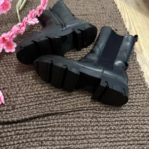Svarta chunky chelsea boots i skinn - Svarta chelsea boots med chunky sula och dragkedja på insidan. Tillverkade i skinn med elastiska paneler på sidorna för enkel påtagning. Runda tår och robust design som ger en cool och edgy vibe till outfiten.