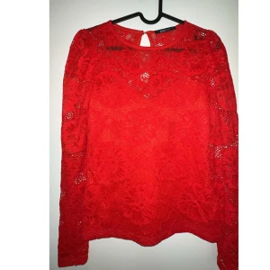 Röd spetsblus från Gina Tricot - En elegant röd spetsblus från Gina Tricot med blommönster. Blusen har långa ärmar och en rund halsringning med en liten öppning i ryggen. I bra skick!