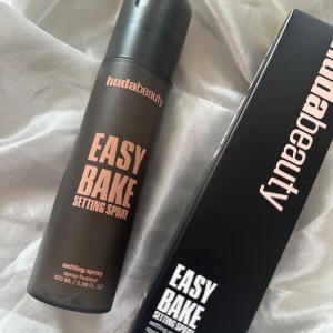Huda Beauty Easy Bake Setting Spray - Huda Beauty Easy Bake Setting Spray i svart matt flaska med rosa text. Innehåller 100 ml och kommer i originalkartong. Perfekt för att fixera sminket och ge en fräsch finish hela dagen. Enkel att använda med praktisk sprayfunktion.