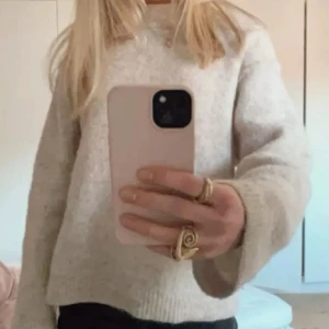 Beige stickad tröja med vida ärmar - Mysig beige stickad tröja med rund hals och vida, långa ärmar. Perfekt för lager-på-lager och passar till både jeans och kjol. Enkel och stilren design som är lätt att matcha med andra plagg. Bilden är lånad från Pinterest.