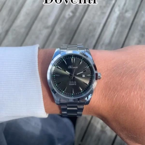 Silverfärgad Doventi klocka med svart urtavla - Stilren klocka från Doventi med svart urtavla och datumvisning. Boetten och länken är i blankt silverfärgat metall, vilket ger en klassisk och clean look. Perfekt accessoar för dig som gillar enkel och tidlös design.