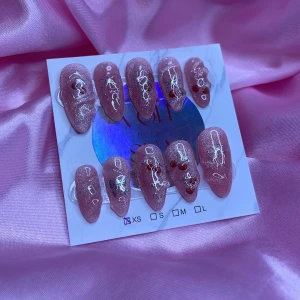 Ch3rryX (XS);Medium Almond - Snygga y2k gelé lösnaglar i rosa med cateye och glittereffekt och unika vita linjemönster samt små röda detaljer. Naglarna har en medium mandelformad design. Perfekt för dig som vill ha en cool och trendig look utan att gå till salong. Kommer i storlek XS: 14 mm, 11 mm, 11,5 mm, 10 mm, 8 mm  