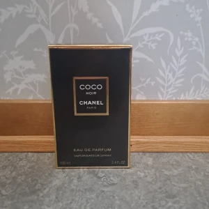 Chanel Coco Noir Eau de Parfum 100ml - Lyxig parfym från Chanel, Coco Noir Eau de Parfum i en elegant svart flaska med guldiga detaljer. Flaskan är fyrkantig med en stilren svart kork och klassisk Chanel-logga. Doften är sensuell och sofistikerad, perfekt för dig som gillar exklusiva parfymer.