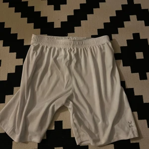 Vita träningsshorts från SOC - Snygga vita träningsshorts från SOC med elastisk midja och enkel design. Perfekta för sport eller gym, tillverkade i ett lätt och smidigt syntetmaterial som andas. Klassisk passform och diskret logga på benet. Riktigt sköna att röra sig i!