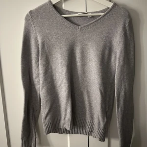 Grå v-ringad stickad tröja  - Mjuk och enkel grå stickad tröja från VILA med v-ringning och ribbade muddar vid ärmslut och nederkant. Perfekt baströja med lång ärm och klassisk passform. Snygg att styla till jeans eller kjol.