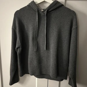 Mörkgrå stickad hoodie - Mysig mörkgrå stickad hoodie från H&M med luva. Tröjan har långa ärmar och bred ribbad kant vid ärmslut och nederkant. Perfekt för kyliga dagar och enkel att matcha med jeans eller leggings.