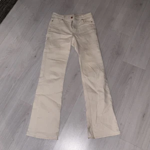 Beiga bootcut jeans med låg midja - Snygga beiga jeans med bootcut-modell och hög midja. Klassisk femficksdesign, dragkedja och knapp framtill. Perfekta för dig som vill ha en stilren och tidlös look. Gjorda i denim-material.