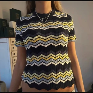 Missoni liknande topp  - Säljer en kortärmad ribbad topp med vågiga ränder i mörkblått, vitt och gult. Toppen har en rund halsringning och ett figurnära snitt med stretchigt material. Perfekt för dig som gillar färg och mönster!
