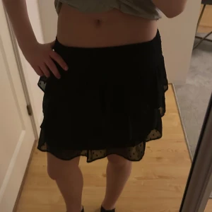 Svart volangkjol med prickigt tyll - Säljer en svart kortkjol med flera lager volanger och ett yttersta lager i prickigt tyll. Resår i midjan för skön passform. Ganska gammal kjol men inte använd så många gånger !!