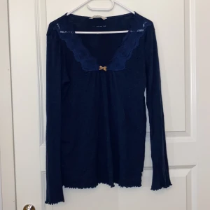 Mörkblå långärmad topp med spets från Odd Molly - Säljer en mörkblå långärmad topp från Odd Molly med spetsdetaljer längs den v-ringade urringningen och en liten beige rosett framtill. Materialet är ribbat och toppen har vågiga kanter vid ärmslut och nederkant. Den säljs inte längre och pris kan diskuteras 💗