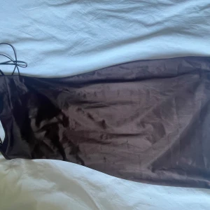 Mörkbrun långklänning med tunna axelband från H&M - Säljer en elegant mörkbrun långklänning med tunna axelband och slimmad passform. Klänningen har en stilren design och är tillverkad i ett glansigt, mjukt material som ger en lyxig känsla.