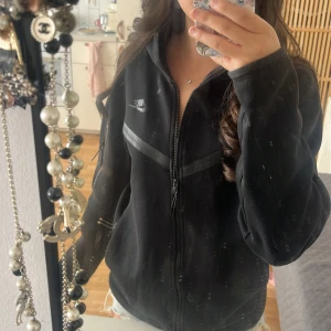Svart nike tech fleece - Svart nike tech fleece med dragkedja framtill och gråa detaljer över bröstet. Jättefin jacka, säljer  den då den inte kommer till användning :).                     Pris kan diskuteras!