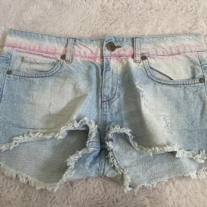 Low waist jeansshorts - Säljer ett par jättefina ljusblå low waist jeansshorts med rosa detaljer upptill. Storlek 34 men jag tycker dom är stora i storlek