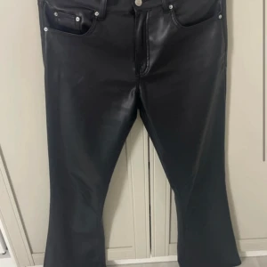 Svarta skinnbyxor från Gina Tricot - Snygga svarta skinnbyxor från Gina Tricot med bootcut-modell. Byxorna har klassisk femficksdesign, dragkedja och knapp framtill. Materialet är syntetiskt skinn med mjuk insida för extra komfort.