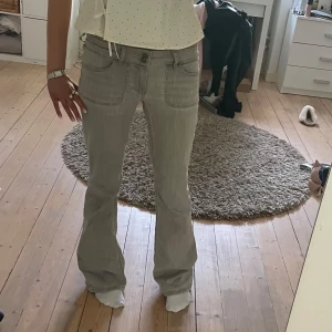 Ljusgrå bootcut jeans - Säljer ett par ljusgrå bootcut jeans med låg midja. Jeansen har klassiska fem fickor och stängs med dragkedja och knapp. Perfekta för dig som gillar en retroinspirerad look med utsvängda ben. Jeansen är lite slitna längst hälen men verkligen inget man tänker på💞