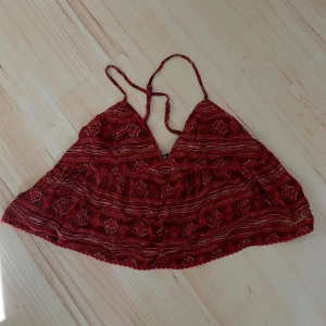 linnetopp från Superdry - Säljer en röd croppad linnetopp från Superdry med tunna axelband och etniskt inspirerat mönster i vitt och rött. Perfekt till varma dagar och enkel att matcha med jeans eller kjol. Sytt lite på ena sidan då bandet satt lite löst, men inget som syns! Kom med bud!