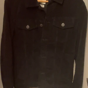 Svart manchesterjacka från Selected Homme - Säljer en svart manchesterjacka från Selected Homme. Jackan har klassisk krage, två bröstfickor med knappar och stängs med knappar framtill. Perfekt för dig som gillar stilrena och tidlösa plagg.