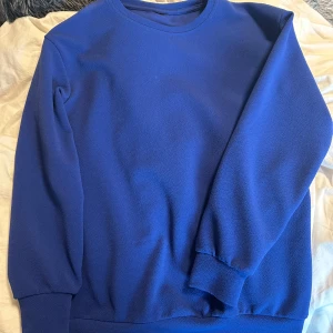 Blå sweatshirt - En enkel blå sweatshirt med rund hals och långa ärmar. Tröjan har en mjuk, lite strukturerad yta och ribbade muddar vid ärmslut och nederkant. Perfekt för en avslappnad stil.