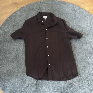 Brun kortärmad skjorta från H&M, aldrig använd! - Säljer en brun kortärmad skjorta från H&M i regular fit. Skjortan har klassisk krage, vita knappar framtill och en bröstficka. Perfekt för varma dagar och enkel att styla till olika outfits. Skriv ifall ni vill ha mer information😀!